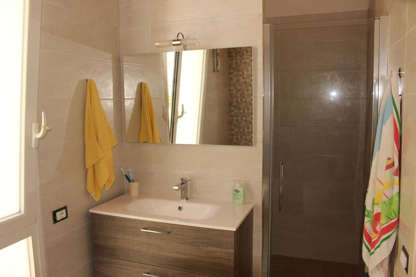 Il bagno con il lavabo, lo specchio, la doccia e gli asciugamani.