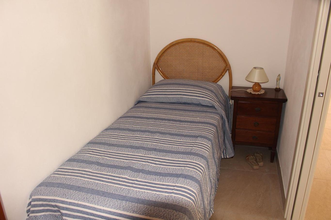 La cameretta con il letto singolo, la testiera di vimini e il comodino.
