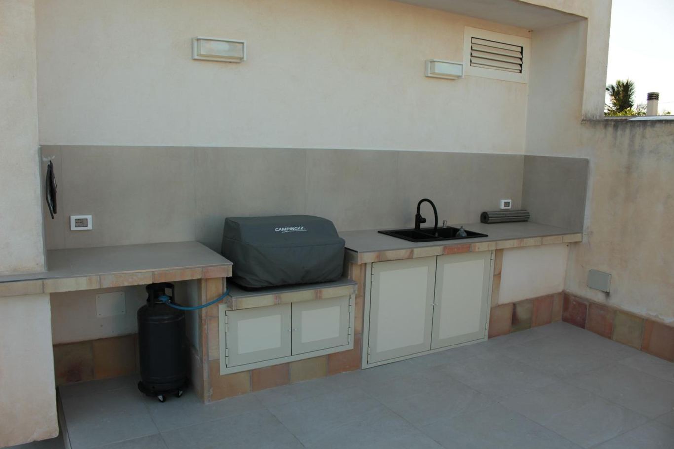 La cucina esterna in muratura con il barbecue, il lavello e gli sportelli chiari.