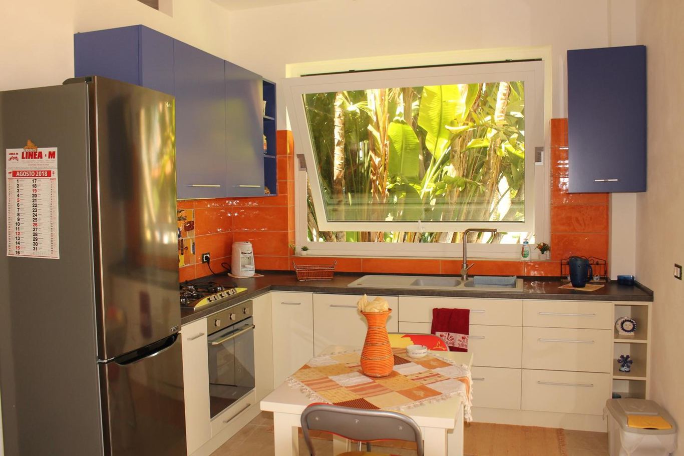 La cucina con il frigorifero, il forno, il piano cottura e la finestra sul giardino.