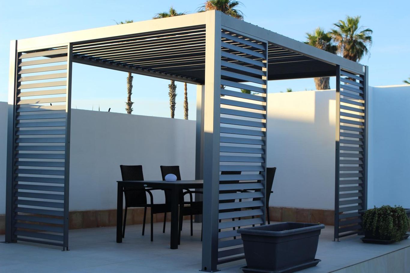 La pergola con le lamelle, il tavolo e le sedie sul solarium bianco.