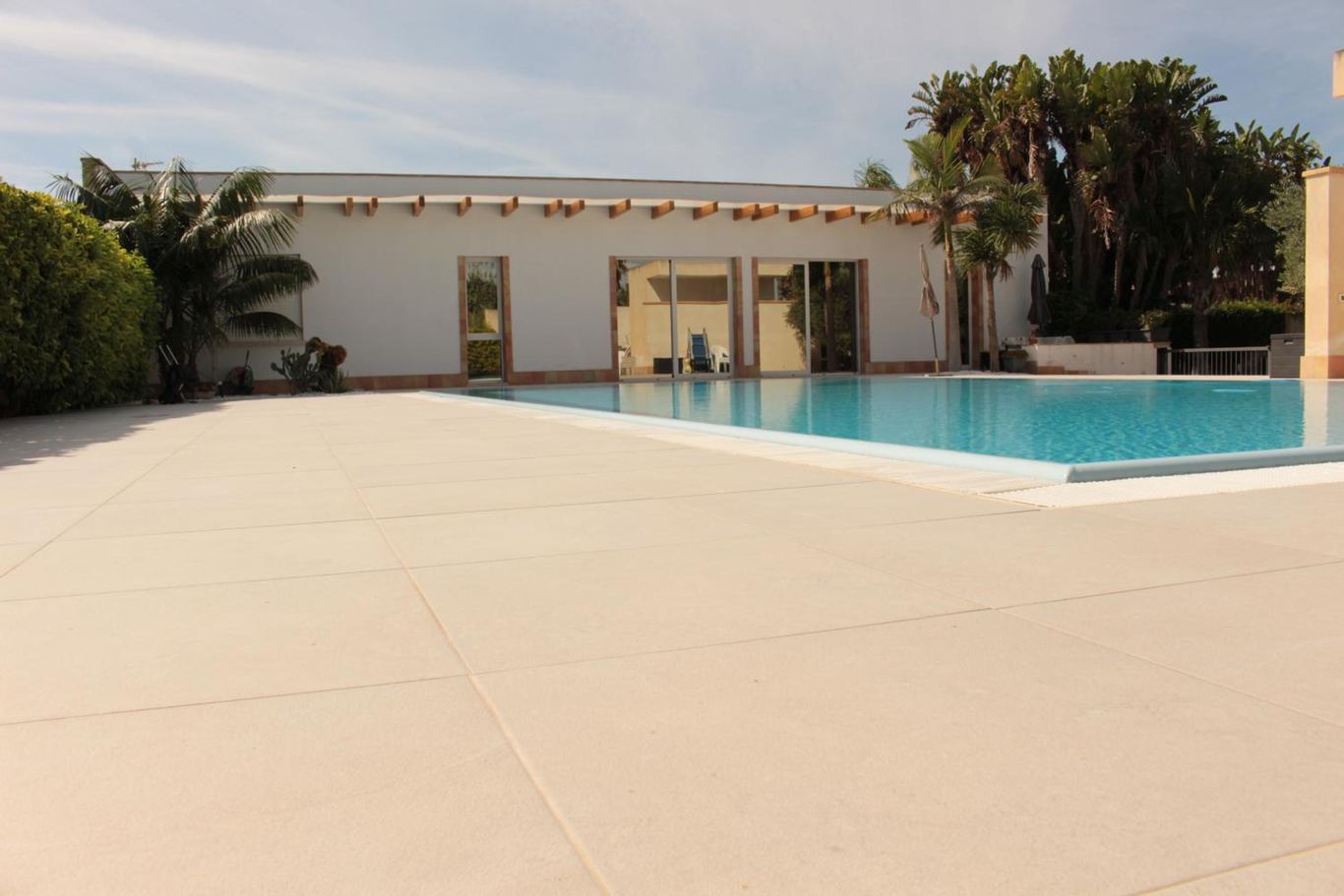 La piscina e la villetta nella luce dell'alba, con le palme e le siepi.