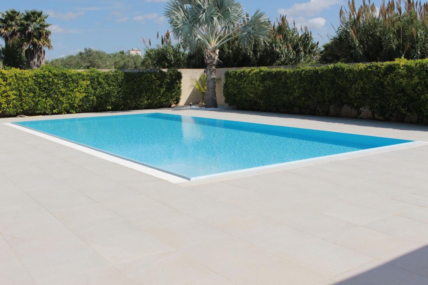 La piscina azzurra e la siepe del giardino sotto il cielo di Marsala.