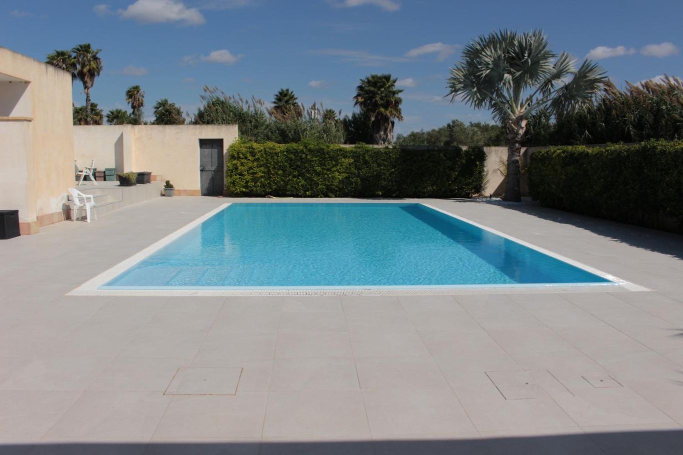 La piscina con le palme, il muro bianco e il cielo con le nuvole.