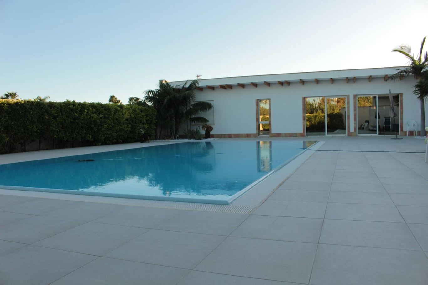 La piscina rettangolare e l'ampio solarium di piastrelle chiare davanti alla villetta.