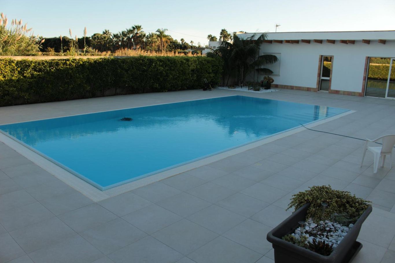 La piscina con le fioriere scure sul bordo del solarium e la villetta in fondo.